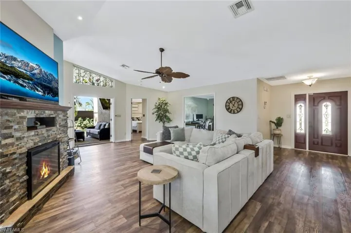 Living room with dark wood-type flooring, ceiling fan, lofted ceiling, and a fireplace