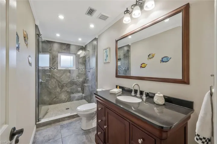 Bathroom with tile patterned floors, toilet, ornamental molding, vanity, and a shower with door