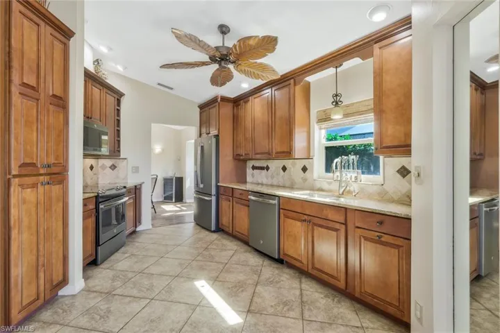Kitchen with sink, appliances with stainless steel finishes, pendant lighting, ceiling fan, and decorative backsplash