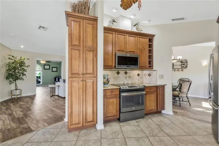 Kitchen featuring vaulted ceiling, light tile patterned floors, appliances with stainless steel finishes, ceiling fan, and decorative backsplash
