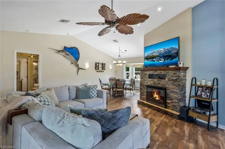 Living room with lofted ceiling, dark wood-type flooring, ceiling fan with chandelier, and a stone fireplace