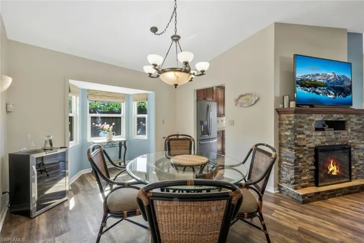 Dining space featuring a stone fireplace, dark hardwood / wood-style floors, lofted ceiling, wine cooler, and an inviting chandelier