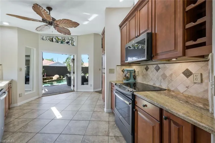 Kitchen with ceiling fan, backsplash, stainless steel appliances, light stone countertops, and light tile patterned flooring