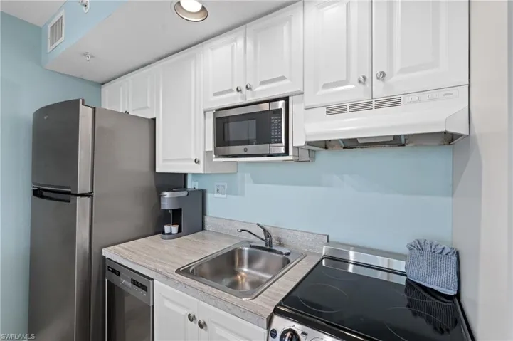 Kitchen with under cabinet range hood, light countertops, a sink, appliances with stainless steel finishes, and white cabinetry