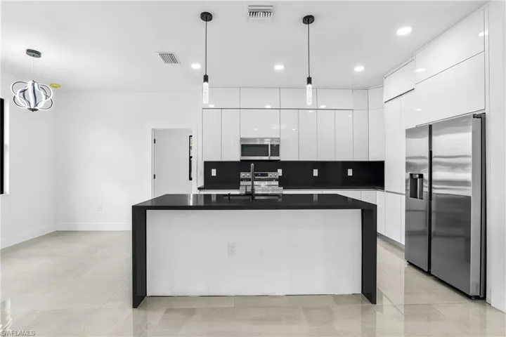 Kitchen featuring pendant lighting, backsplash, appliances with stainless steel finishes, a center island with sink, and white cabinets