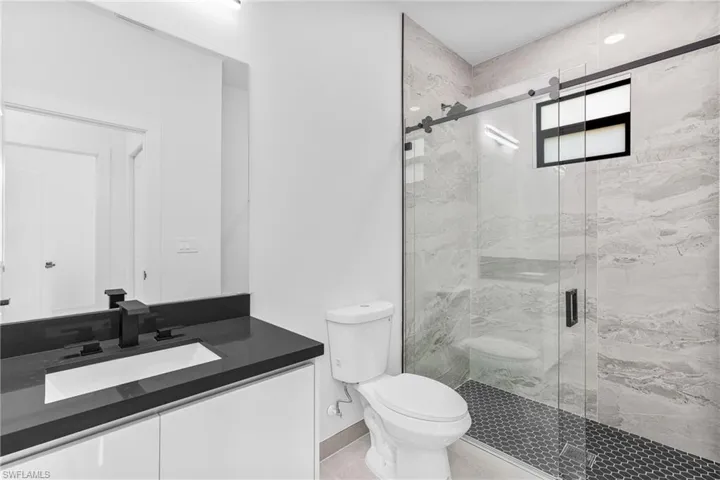 Bathroom with a shower with shower door, toilet, vanity, and tile patterned floors
