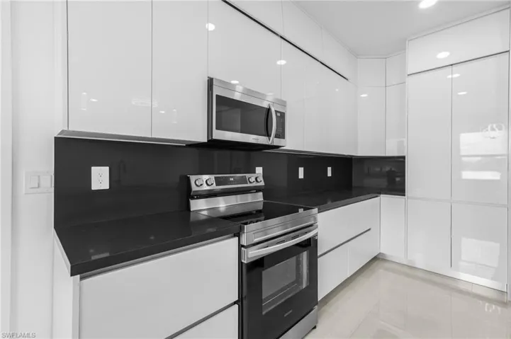 Kitchen with light tile patterned floors, white cabinetry, backsplash, and stainless steel appliances