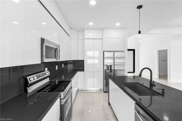 Kitchen with stainless steel appliances, sink, decorative light fixtures, and white cabinetry