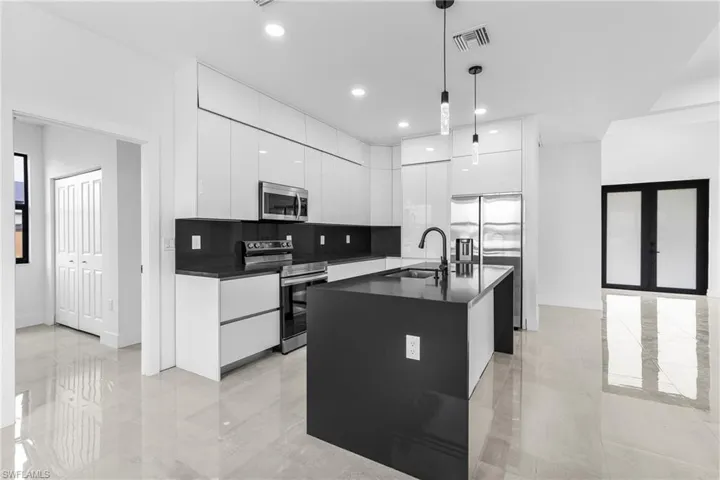 Kitchen with appliances with stainless steel finishes, tasteful backsplash, a kitchen island with sink, hanging light fixtures, and white cabinetry