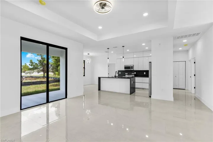 Kitchen with decorative light fixtures, appliances with stainless steel finishes, a kitchen island with sink, sink, and white cabinetry