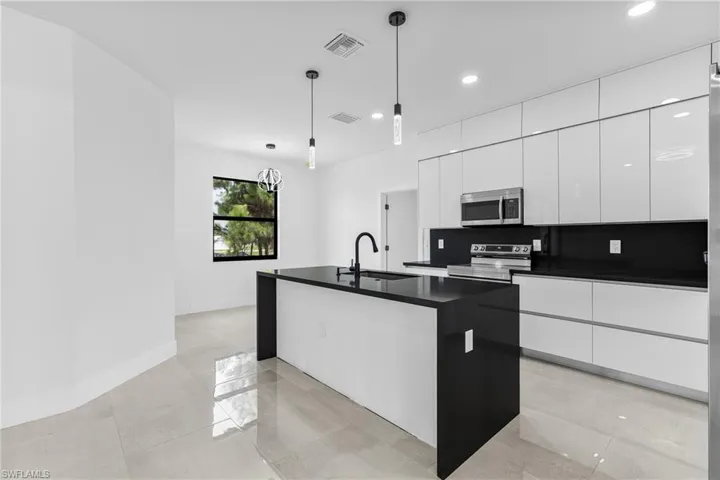 Kitchen featuring hanging light fixtures, sink, an island with sink, decorative backsplash, and appliances with stainless steel finishes