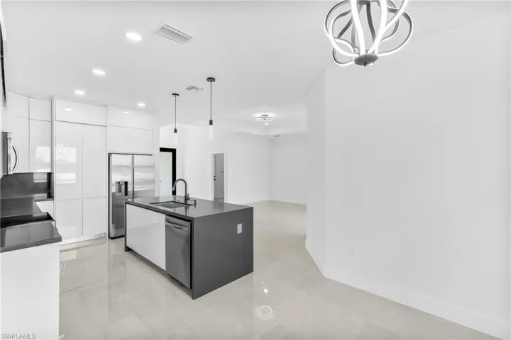 Kitchen featuring white cabinets, hanging light fixtures, appliances with stainless steel finishes, sink, and an island with sink