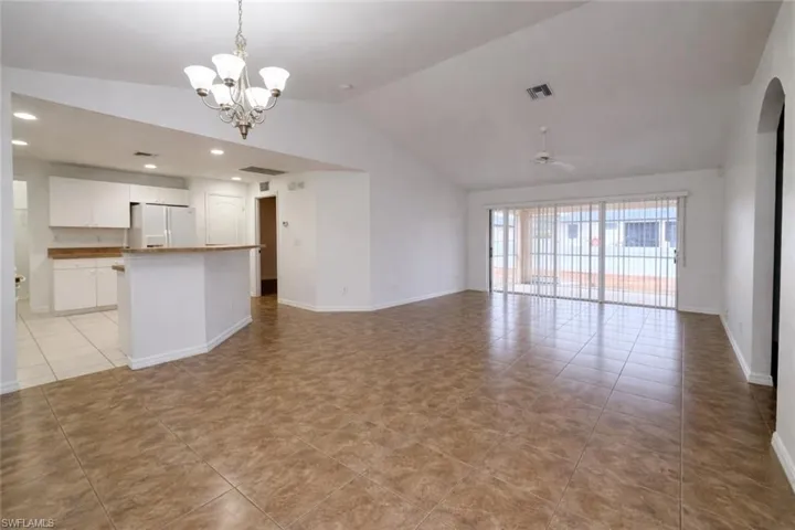 Unfurnished living room with lofted ceiling, a chandelier, light tile patterned flooring, and ceiling fan