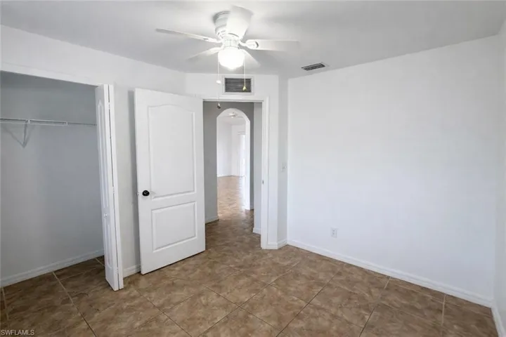 Unfurnished bedroom featuring arched walkways, a ceiling fan, and a closet