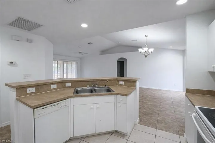 Kitchen with white cabinetry, white dishwasher, lofted ceiling, a ceiling fan, and a center island with sink