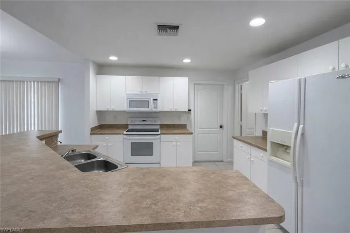 Kitchen with white appliances, white cabinets, recessed lighting, and light tile patterned floors