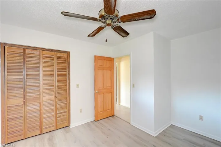 Unfurnished bedroom with ceiling fan, a textured ceiling, a closet, and light hardwood / wood-style flooring