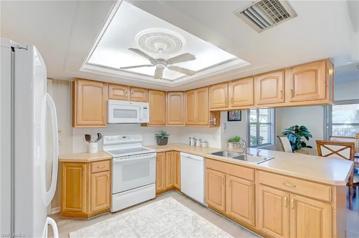 Kitchen featuring light brown cabinetry, sink, ceiling fan, kitchen peninsula, and white appliances