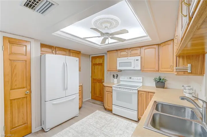 Kitchen featuring sink, tasteful backsplash, white appliances, light brown cabinets, and ceiling fan