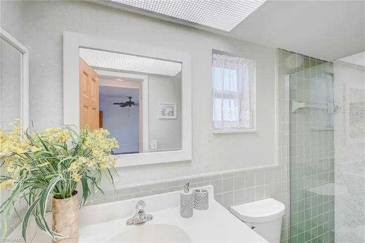 Bathroom with a tile shower, sink, tile walls, ceiling fan, and toilet