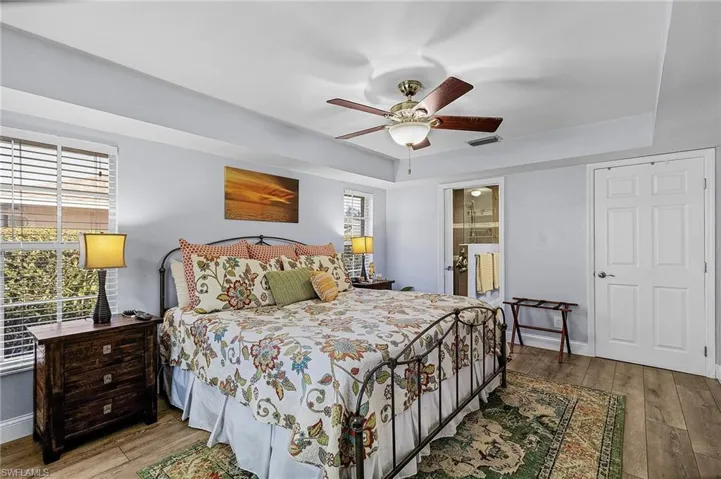 Bedroom featuring a raised ceiling, wood-type flooring, connected bathroom, and ceiling fan