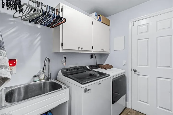 Clothes washing area featuring cabinets, washer and clothes dryer, sink, and hardwood / wood-style floors