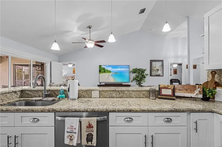 Kitchen featuring vaulted ceiling, dishwasher, white cabinetry, sink, and light stone countertops