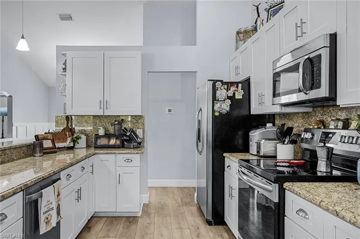 Kitchen with white cabinetry, appliances with stainless steel finishes, decorative light fixtures, and light hardwood / wood-style floors