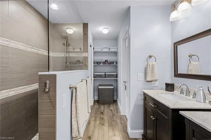 Bathroom with tiled shower, vanity, and wood-type flooring
