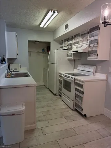 Kitchen featuring white appliances, upper and lower cabinetry with distressed wood-look accents, a stainless steel sink, and wood-finish flooring