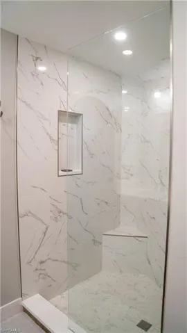 Glass-enclosed shower featuring white and gray veined tile walls