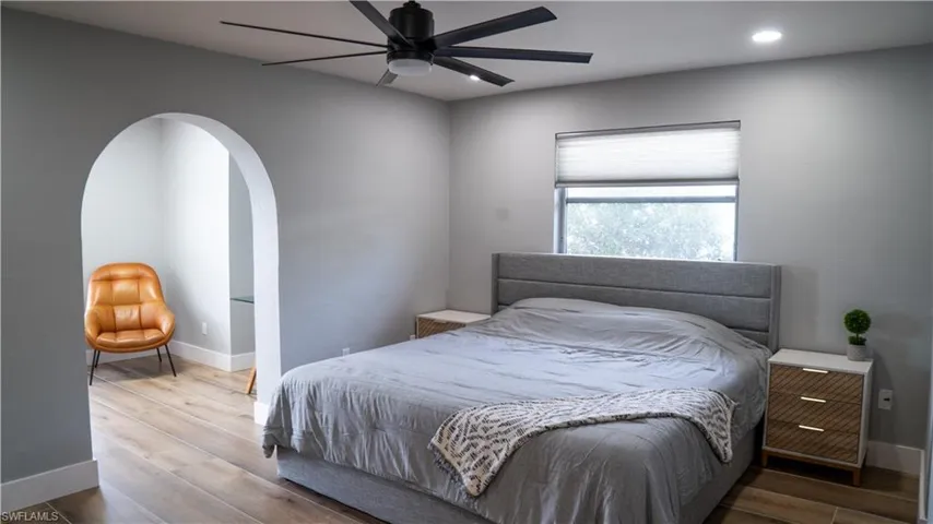 Bedroom featuring an arched doorway, wood-finish flooring, a contemporary ceiling fan, recessed lighting, and a window with a cellular shade