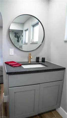 Contemporary vanity featuring a dark countertop, an undermount sink, and a gold-finish faucet