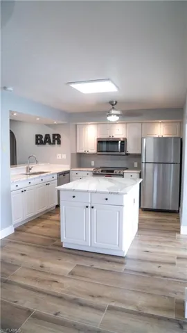 Kitchen featuring white shaker cabinetry, stainless steel appliances, a central island with countertop, wood-finish flooring, and a subway tile backsplash