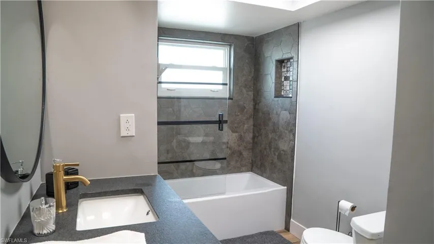 Bathroom featuring a tub/shower combination with hexagonal wall tile, a built-in shower niche, and a window