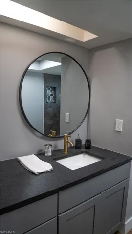 Modern vanity with a dark countertop, an undermount sink, and a gold-finish faucet