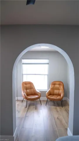 Arched entryway leading to a room with wood-finish flooring, light gray walls, and a window with blinds