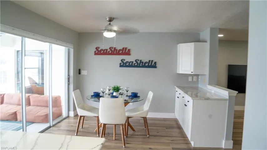 Sliding glass doors opening to an outdoor area with seating, wood-finish flooring, a ceiling fan with light fixture, and white cabinetry with a light-toned countertop