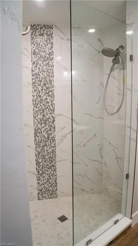 Walk-in shower featuring a frameless glass enclosure, large format white marble-look wall tiles, and a mosaic tile accent strip
