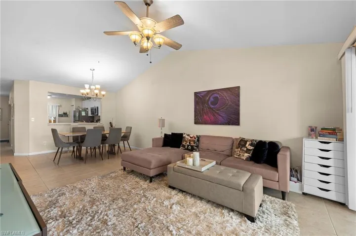 Living room featuring light tile patterned floors, vaulted ceiling, and ceiling fan with notable chandelier