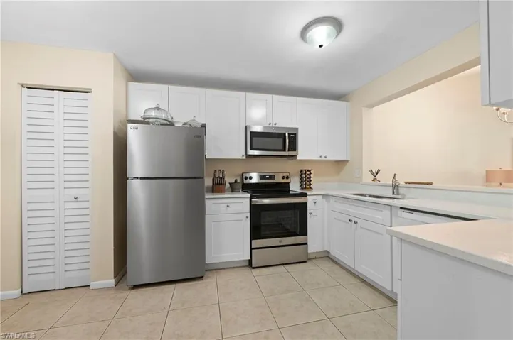 Kitchen featuring white cabinets, light tile patterned floors, stainless steel appliances, and sink