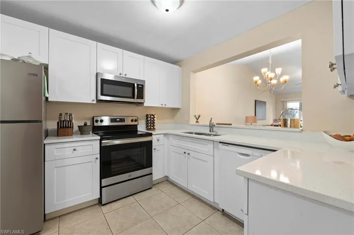 Kitchen with white cabinets, stainless steel appliances, a notable chandelier, and sink
