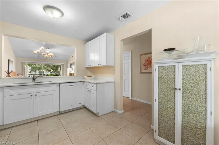 Kitchen featuring light tile patterned floors, white dishwasher, sink, vaulted ceiling, and white cabinets