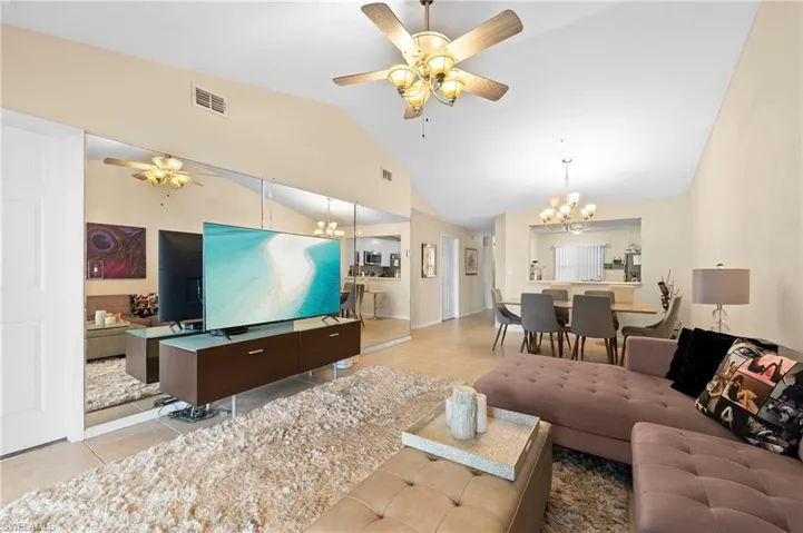Tiled living room with ceiling fan with notable chandelier and high vaulted ceiling