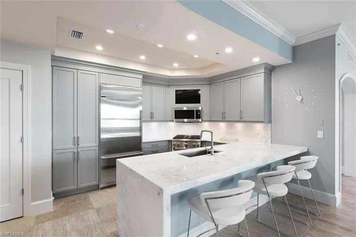 Kitchen featuring gray cabinetry, a breakfast bar area, light stone countertops, a peninsula, and stainless steel appliances