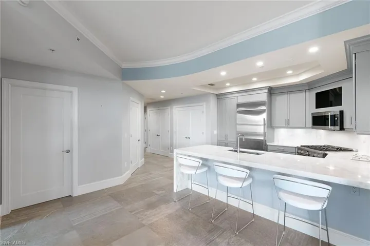 Kitchen with light stone counters, crown molding, a peninsula, a kitchen breakfast bar, and gray cabinetry