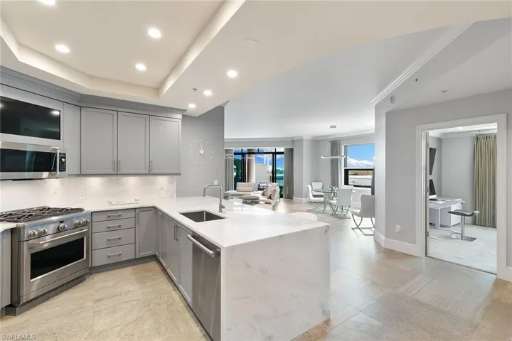 Kitchen with gray cabinets, a peninsula, light stone countertops, stainless steel appliances, and recessed lighting