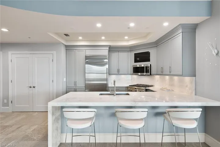 Kitchen with light stone countertops, a breakfast bar area, a peninsula, recessed lighting, and a raised ceiling