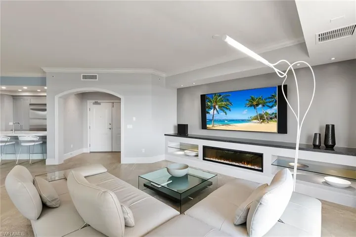 Living room with arched walkways, a glass covered fireplace, crown molding, and recessed lighting