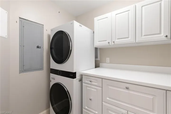 Laundry area with stacked washer and dryer, electric panel, and cabinet space